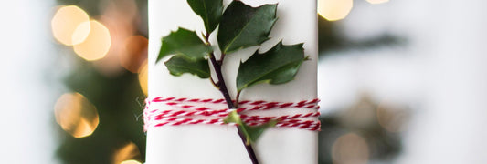 A small present wrapped in white paper with red and white twine, with a holly sprig tucked in it